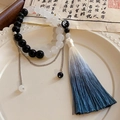 Macro detail of beaded bracelet with Yin Yang charm and blue gradient silk tassel - Black-White