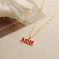 Collier vintage doré avec pendentif LOVE en émail rouge et tulipe sur un fond beige texturé - Lettres LOVE / Rouge