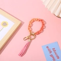 Orange matte chain bracelet keychain with pink tassel and golden metal clasp on desk - Orange + Tangerine