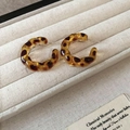 Dettaglio ravvicinato di orecchini a cerchio tartarugati in una scatola di velluto bianco - 48# Anello a C Torto / Leopardo Caffè