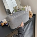 Close-up of silver-gray woven texture cosmetic bag with metallic handle on a vanity desk - Gray