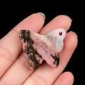 Pink agate butterfly carved stone pendant with black veins held against dark background - Rhodonite