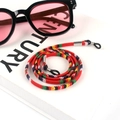 Close-up of bohemian woven eyeglass strap in red ethnic pattern on a white prop book - US 7