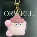 Detailed close-up of a pink fuzzy keychain with a knit hat and cute googly eyes - Pink