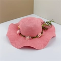 Detail of pink straw sun hat featuring wavy brim and delicate floral rose wreath decoration - Pink