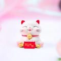 Statuetta di gatto portafortuna bianco con targa rossa su sfondo rosa sfumato - Gatto portafortuna desiderando ricchezza