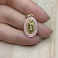 Detail of a gold oval Jesus pendant with pink shell inlay held by a hand on wood - Pink