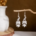 Detailed shot of silver peacock earrings with leaf pendants on a rustic branch - Silver Hollow Peacock Leaf(E2875-05)
