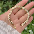 Mano che tiene un bracciale a cuore geometrico placcato in oro con zirconi a pavé - Design a Spirale