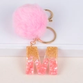 Detail of pink pompom keychain with resin letter M featuring gold glitter and shell flakes - Letter M