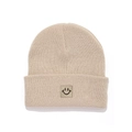 Detail shot of a beige knitted kids beanie featuring a brown square smiley face patch - Beige