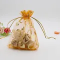 Close-up of orange organza gift bag with gold heart patterns and drawstring closure - Orange