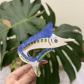 Detailed close-up of a blue acetate fish hair claw clip held against green plants - Blue Marlin