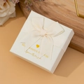 White textured jewelry gift box with a beige ribbon bow and gold lettering - Off-White Swallowtail Bow