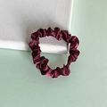 Maroon satin silk hair scrunchie with soft pleats on a textured white display block - Dark Red