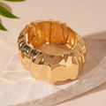 Nahaufnahme des goldenen breiten Armreifs mit Wellentextur auf einer Steinoberfläche - Goldener gefalteter offener Armreif