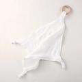 Close-up of white cotton gauze baby comforter with a natural wooden teething ring - White