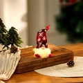 Close-up of a glowing Christmas gnome with LED beard and knit hat on a festive tray - Red Short Leg Style