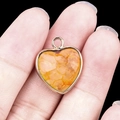 Golden heart pendant with orange agate gemstone held by hand against black background - Yellow Tinted Quartz Gold Edging