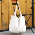 Minimalist white canvas tote bag hanging on a black chair with a rustic wooden background - Off White