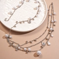 Mehrlagige silberne Kette mit Perlen, Muscheln und Sternenanhängern auf einem Tablett - Silber