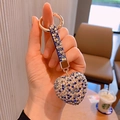 Detailed view of a hand holding a luxury heart-shaped keychain with blue rhinestones - Blue