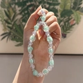 Pastel green acrylic beaded phone strap with iridescent beads shown on a hand - Green White Flower