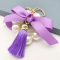 Macro detail of purple ribbon bow and pearl bead tassel keychain with golden metal clasp - Purple