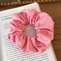 Detailed view of a soft pink pleated fabric scrunchie placed on an open book background - Pink