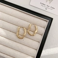 Detailed view of irregular wavy golden hoop earrings on a beige velvet jewelry tray - Gold