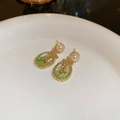 Macro-opname van vintage groene emaille oorbellen met gouden roos en parel detail - Zilveren naald - Gouden ovale roos bloem drop oorbellen