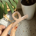Détail d'une pince à cheveux rose poudré en acrylique avec ressort doré tenue à la main - Rose Nude Foncé