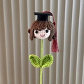 Detail of hand-knitted graduation doll head with a black mortarboard and red tassel - Doctoral Cap Girl