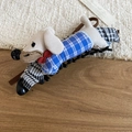 Close-up of plush dachshund hair clip with blue plaid ribbon on textured wood - White-Blue