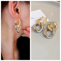 Detail of interlocking gold and silver dual-tone oval hoop earrings on model and table - Chain Stud Style