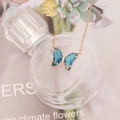 Detailed view of a gold butterfly necklace with blue crystals on a perfume bottle - Deep Lake Blue