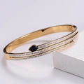 Detalle de brazalete dorado con una gema azul en forma de gota y circonitas cúbicas - Dorado