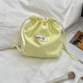 Pale yellow drawstring storage pouch with fabric label and ribbon closure on white fabric - Bright yellow