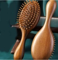 Detailed view of two brown sandalwood massage hairbrushes on a green fabric backdrop - Air Cushion Massage Brush