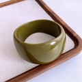 Macro shot of an olive green acrylic resin wide bangle on a textured fabric surface - Olive Green