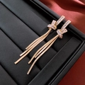 Dettaglio di orecchini dorati a nappa con nodo e zirconi cubici su sfondo di pelle nera - Orecchini a Frangia con Nodi in Zirconia e Perno in Argento / Oro