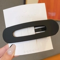 Matte black oversized hair clip with oval hollow design on a white display card - Black