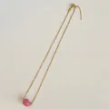 Detalle de una cadena fina dorada con un colgante de frijol rosa liso en fondo blanco - Cadena Universal / Rosa