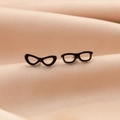 Vista macro di orecchini a lobo a forma di occhiali neri su sfondo in tessuto beige - Nero