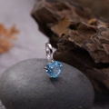Macro shot of S925 silver pendant with blue heart gemstone on a dark smooth pebble - Natural Topaz Heart Pendant Silver