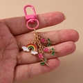 Portachiavi chic in metallo con nuvola arcobaleno e rosa rosa tenuto in mano - Rosa