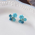Close-up of blue floral earrings with cat eye stones and crystals on white ceramic - Blue