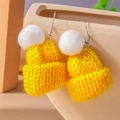 Detail of yellow knitted hat earrings with white pompom on a beige ceramic pot edge - Yellow