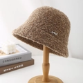 Close-up of caramel teddy wool bucket hat with NN silver metal logo on wooden stand - Mocha