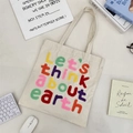 Off-white canvas tote bag featuring colorful chenille earth embroidery on a white desk - Beige